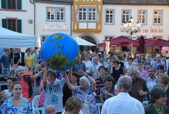 Weltkirchliche Aufgaben/Mission und weltweite Ökumene Fröhliche Menschen feiern im Freien Gottesdienst und reichen sich über die Köpfe hinweg einen großen aufblasbaren Globus weiter